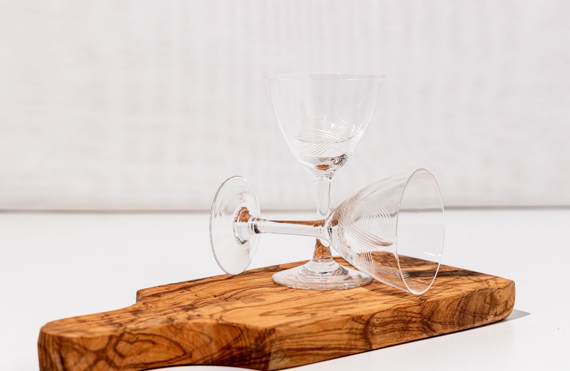 Two elegant crystal glasses placed on a wooden cutting board against a white background.