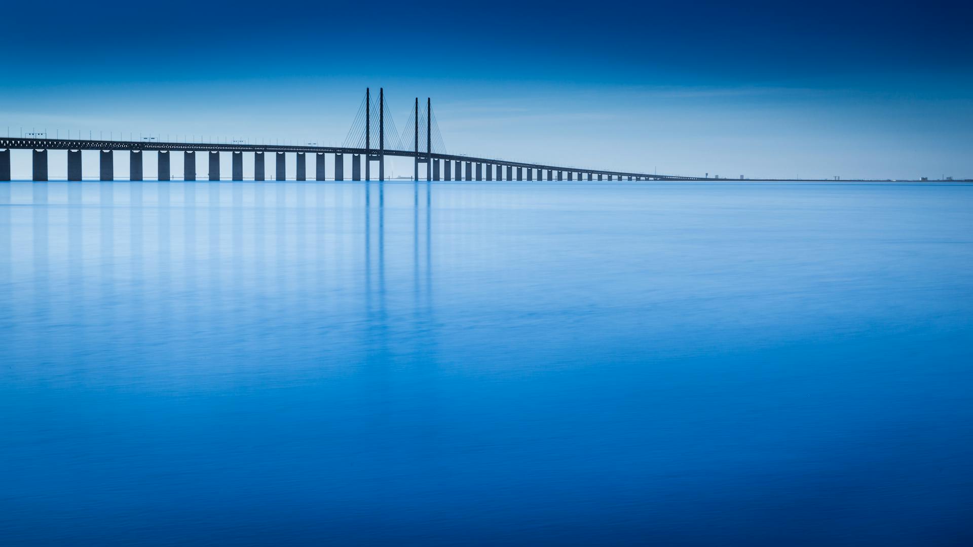 The Oresund Bridge stretches over tranquil blue water under a clear sky connecting Sweden and Denmark.