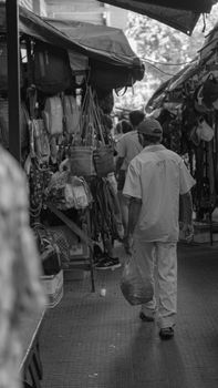 A candid black and white photo of a bustling street market with buyers and stalls.
