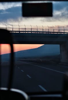 Evening view through a car window under a highway bridge during sunset, conveying tranquility and travel