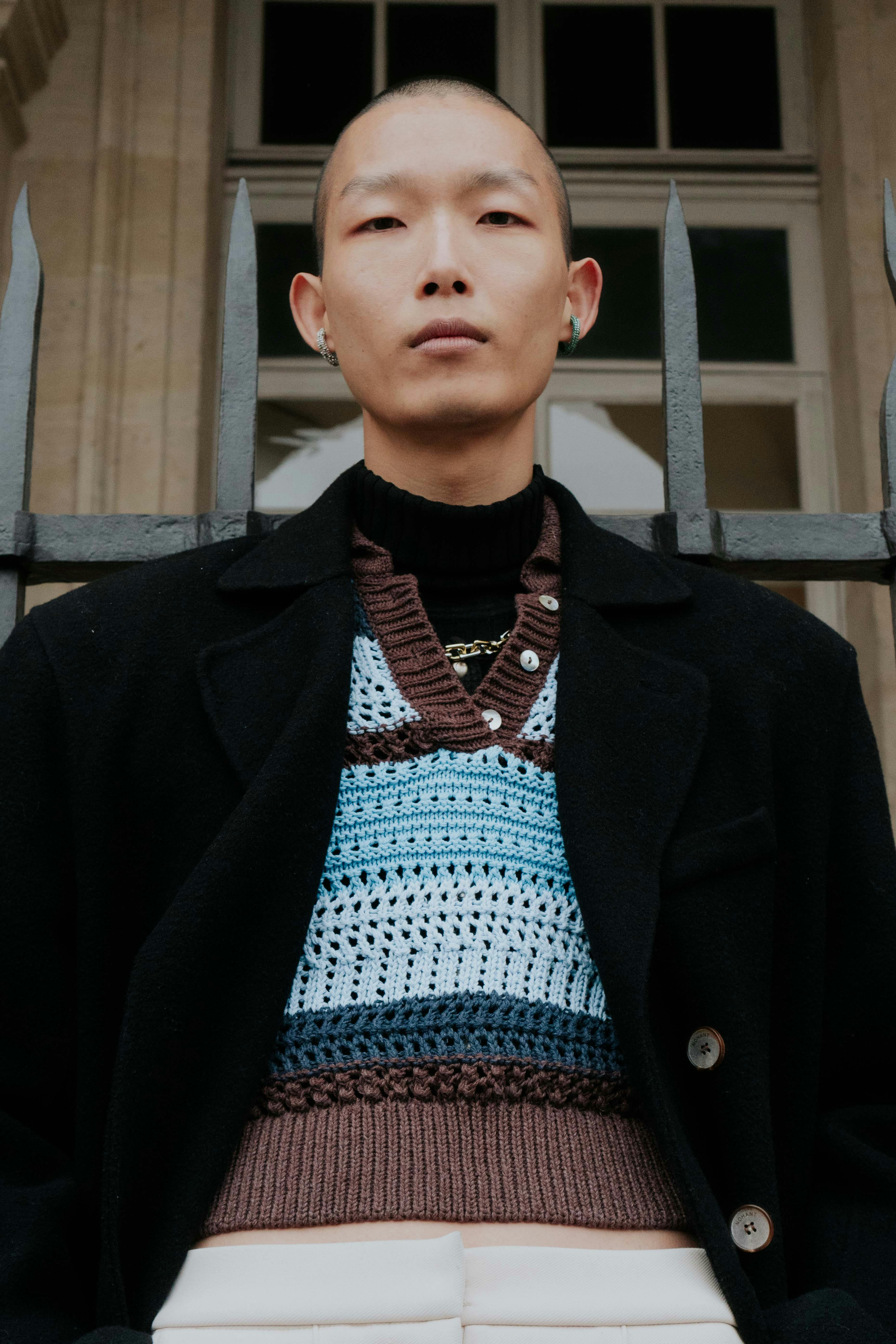 A fashion-forward man poses confidently outdoors in a layered outfit, embodying modern style.