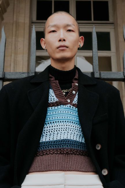 A fashion-forward man poses confidently outdoors in a layered outfit, embodying modern style.