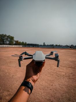 Close-up of a hand holding a drone in an open field, clear sky.