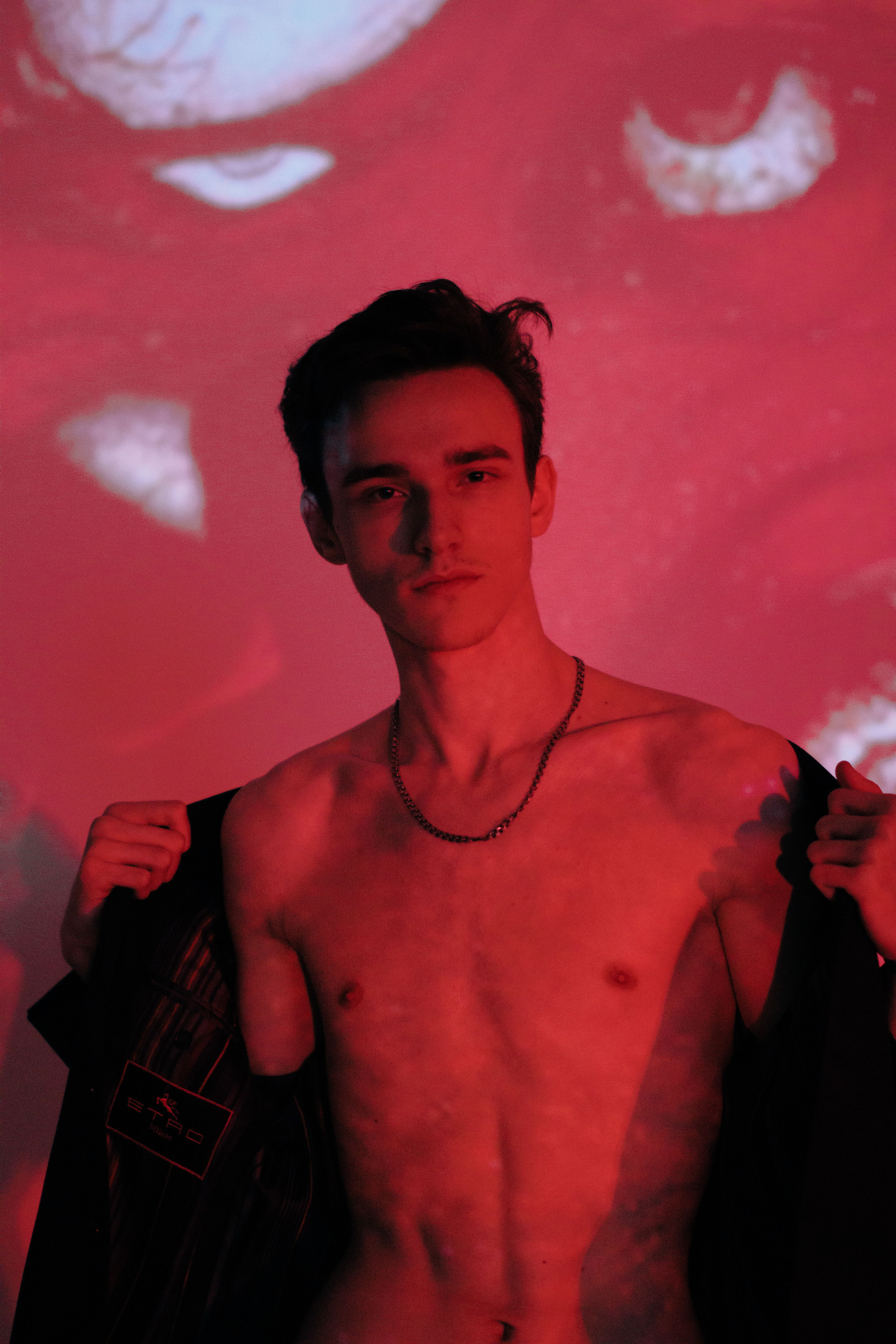 Artistic portrait of a topless young man in moody red lighting, creating a dramatic effect.