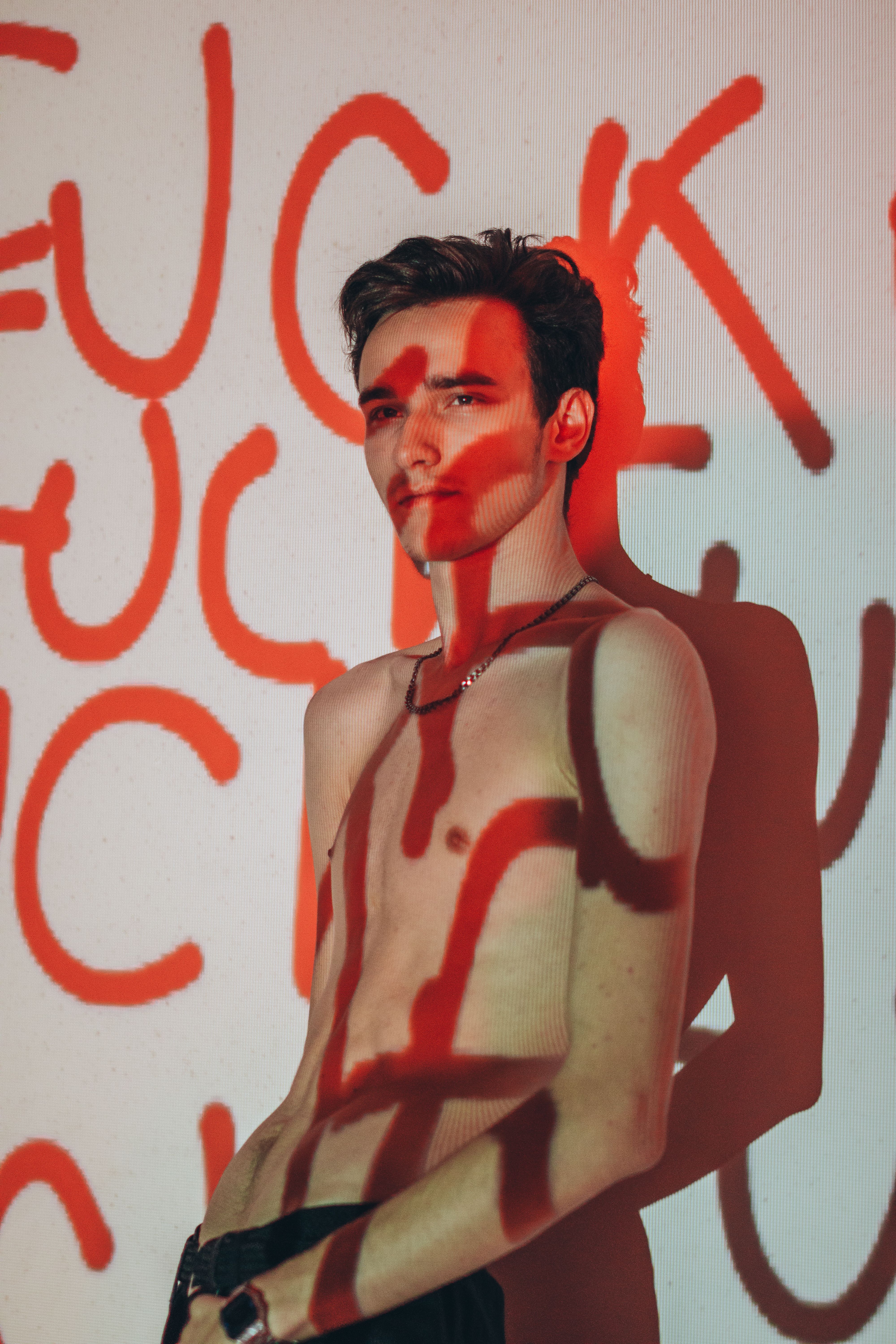 Shirtless young man with red graffiti shadows on his skin in a studio shoot.