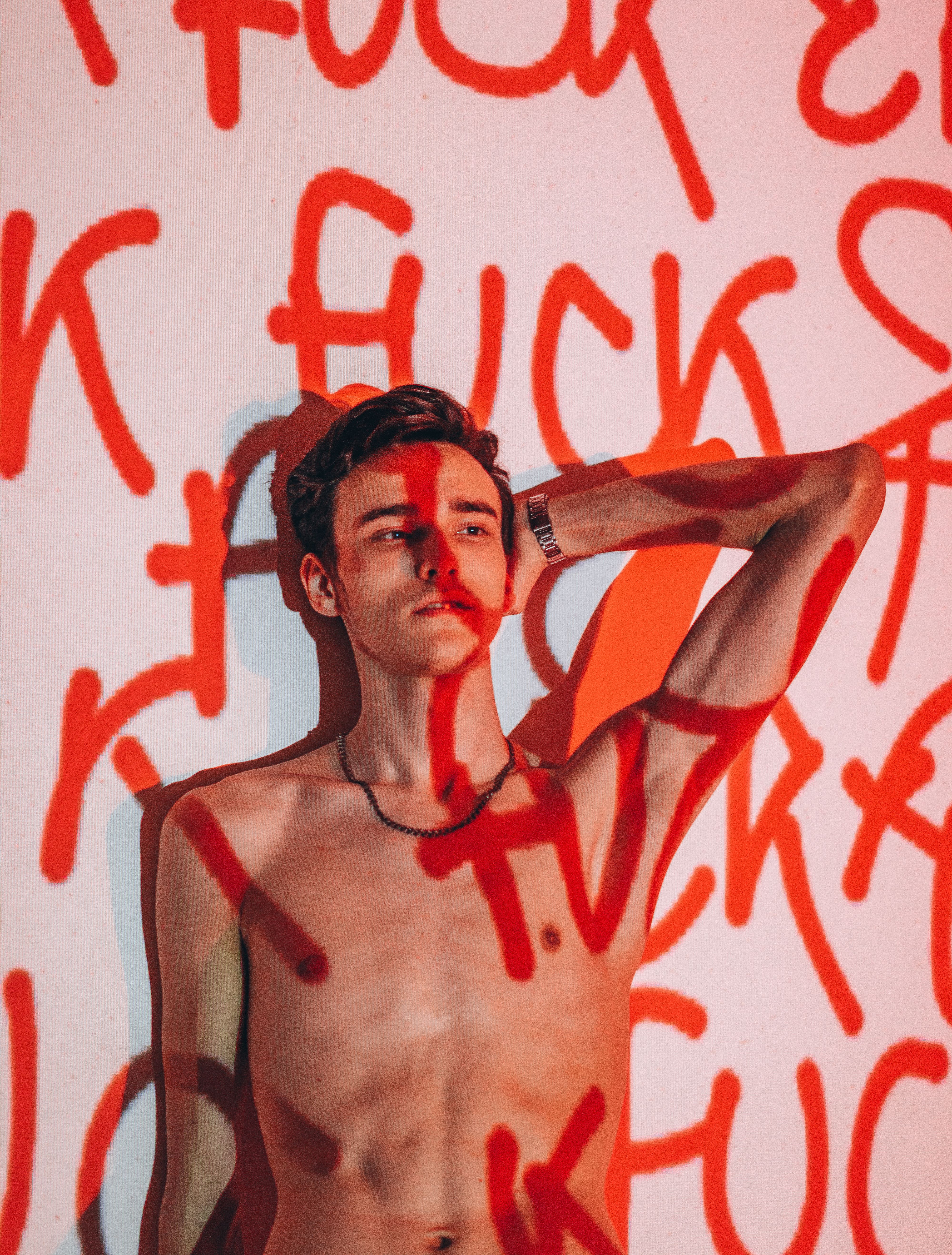 A topless man in front of a red graffiti-like text on a white background, creating a bold artistic statement.