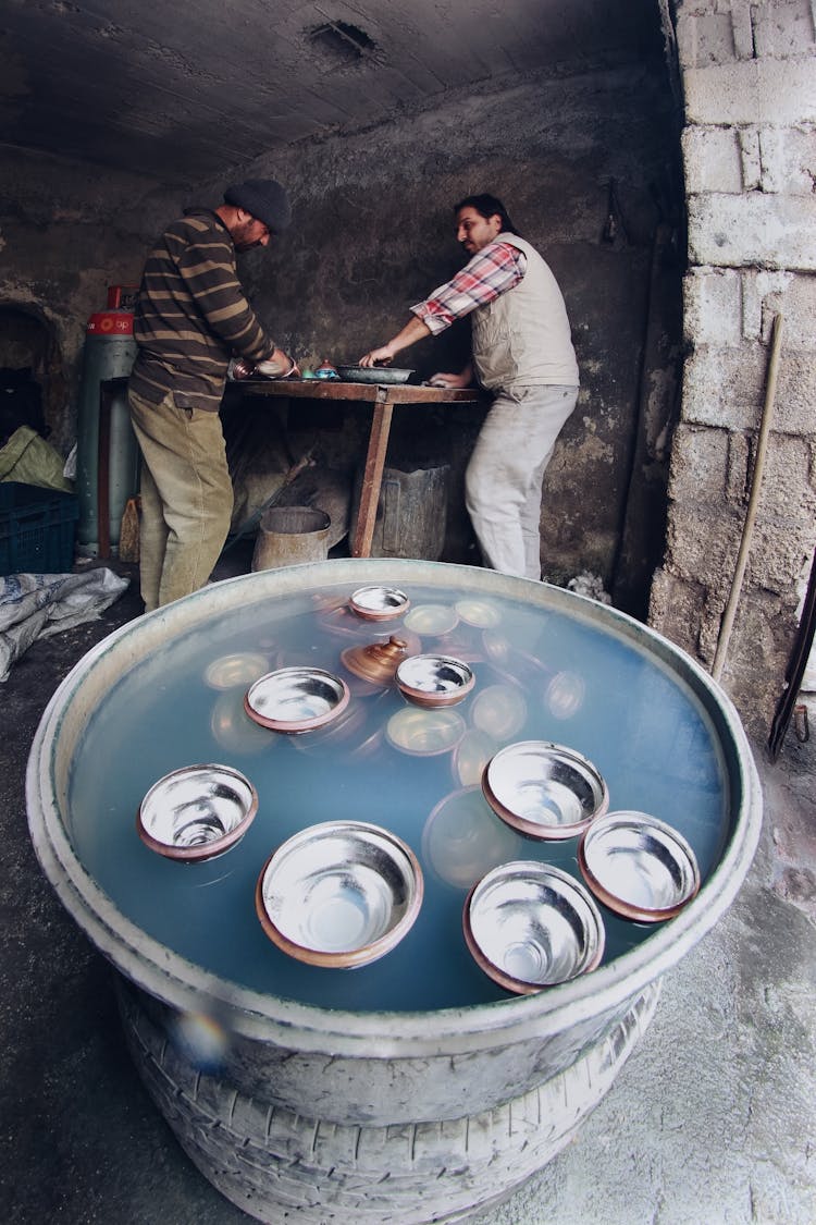 Men In A Craft Studio, And Metal Pots In A Large Basin