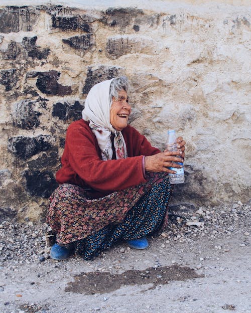 Photo of a Senior Woman Crouching by a Wall and Smiling
