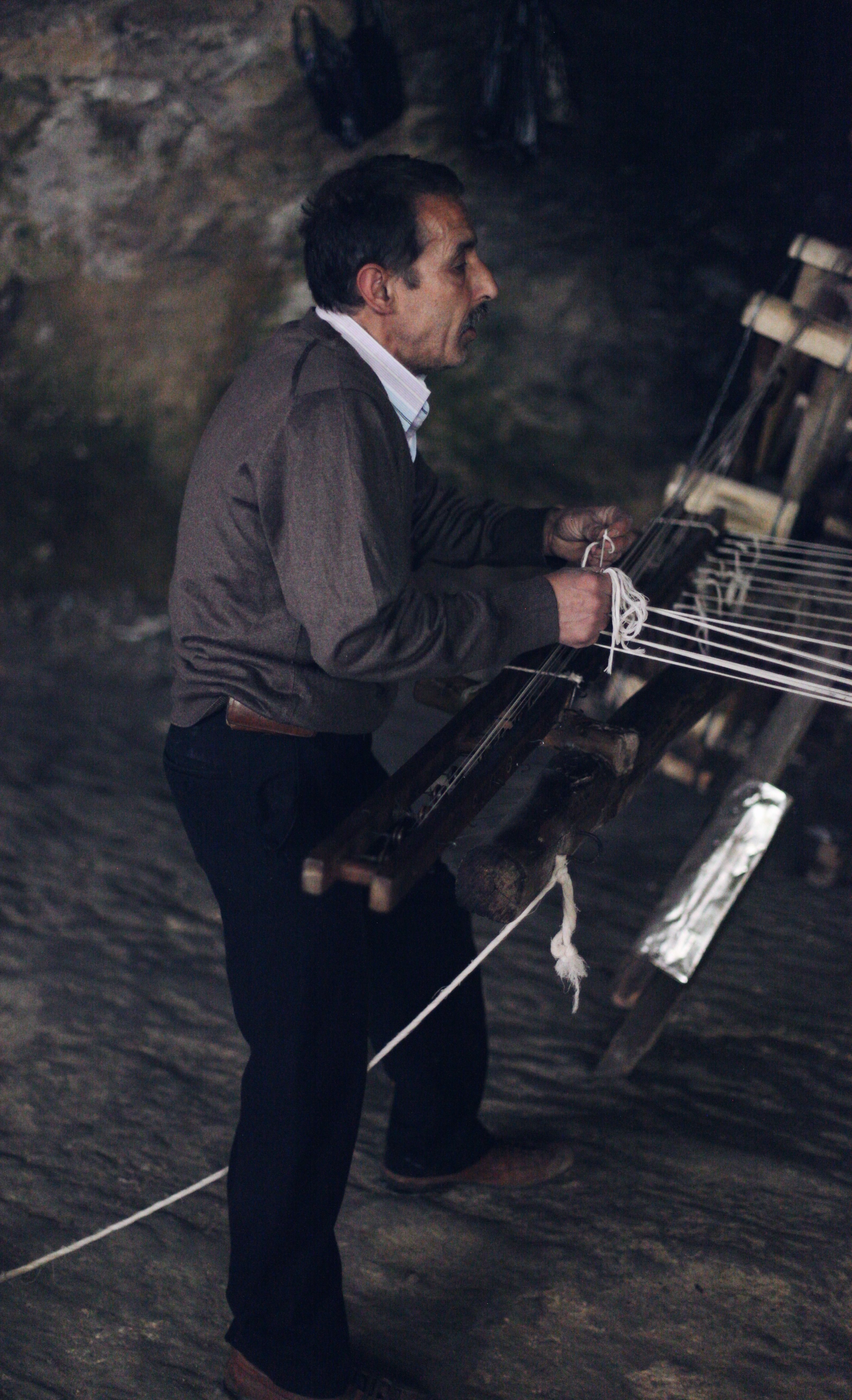 A skilled artisan focused on traditional weaving in a dimly lit workshop.