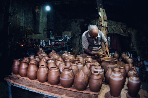 Free Elderly potter skillfully shapes clay in a dimly lit workshop surrounded by handcrafted pots. Stock Photo