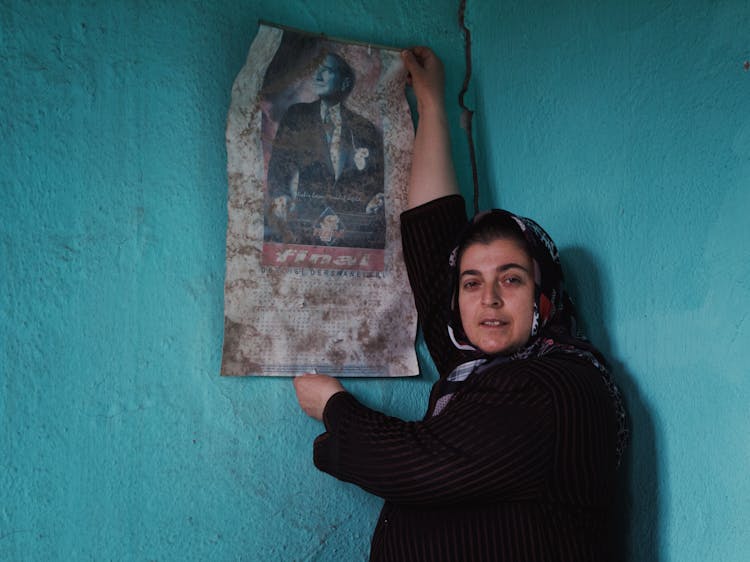 Photo Of A Woman Wearing A Headscarf Holding An Old Calendar Against A Turquoise Wall