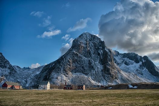 Stunning snowy mountain landscape in Lofoten, Norway, with picturesque houses under a vibrant sky.