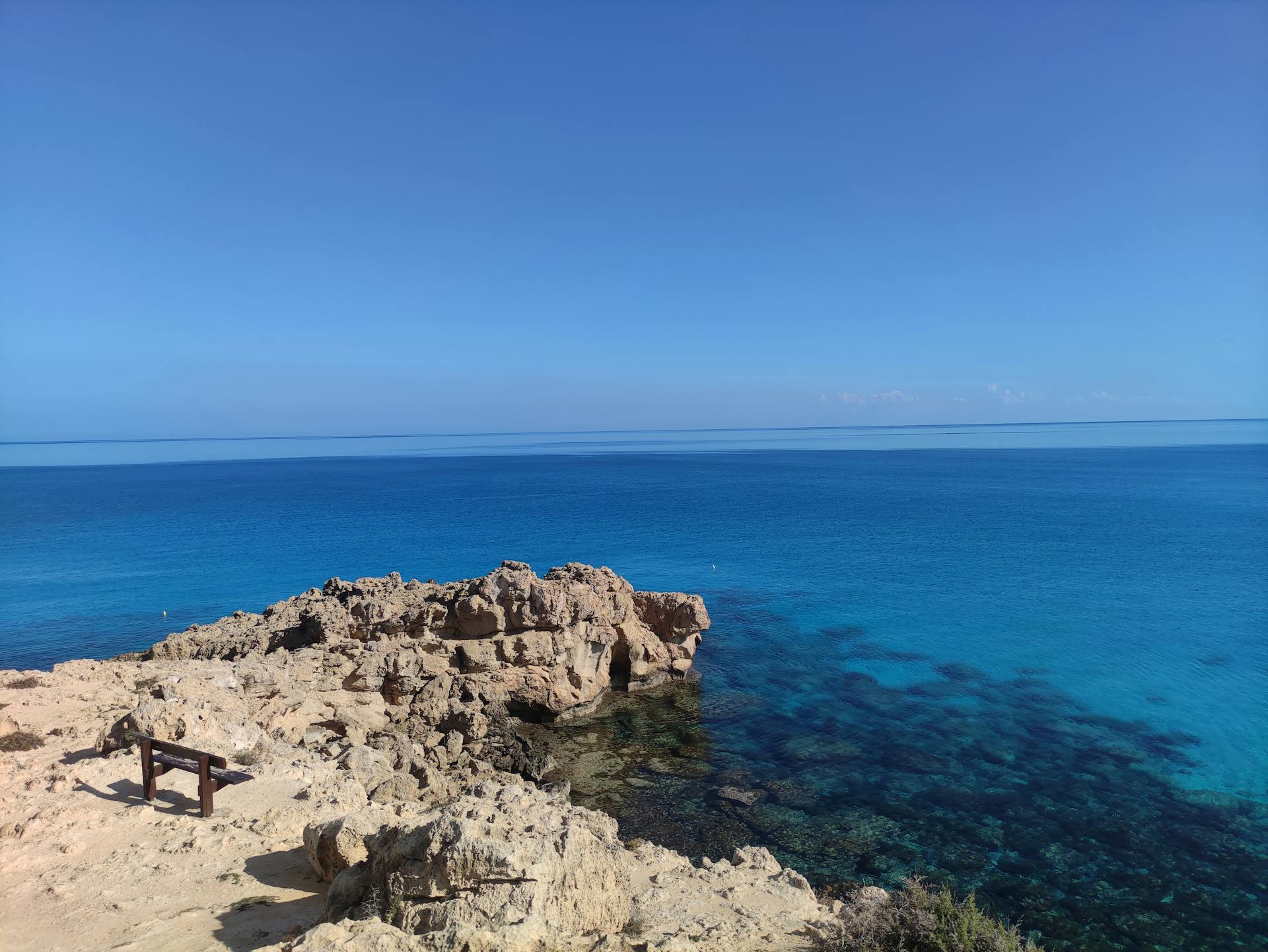 Breathtaking view of a calm azure sea meeting a rocky shore under a clear sky, perfect for discovering tranquility.