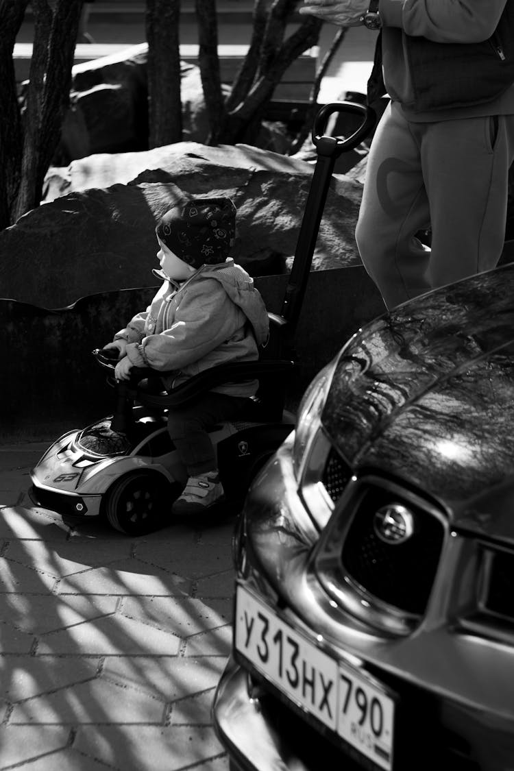 Black And White Photo Of A Child Riding On A Toy Car