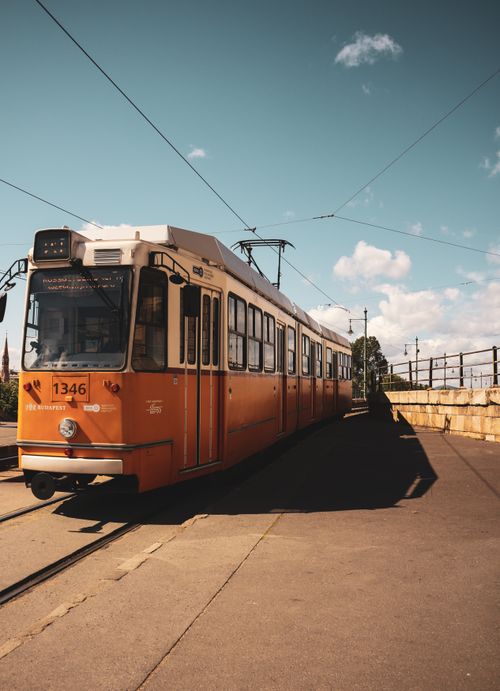 Free A vibrant orange tram travels along the sunlit tracks in Budapest, highlighting urban transit in Hungary. Stock Photo