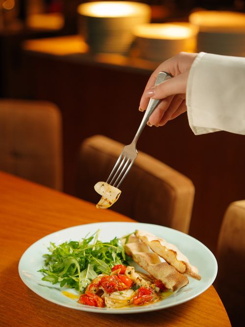 Free Close-up of a hand holding a fork with grilled vegetables over a plate of Mediterranean cuisine. Stock Photo