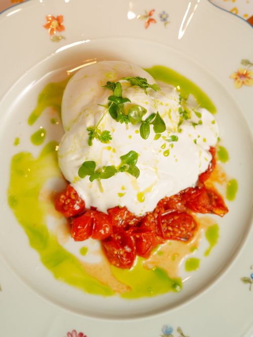 Free Close-up of creamy burrata cheese atop cherry tomatoes garnished with fresh basil on a floral plate. Stock Photo