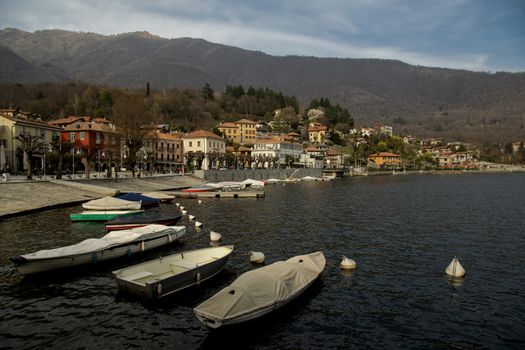 Peaceful scene of Mergozzo Lake's waterfront with moored boats and mountain backdrop in autumn.