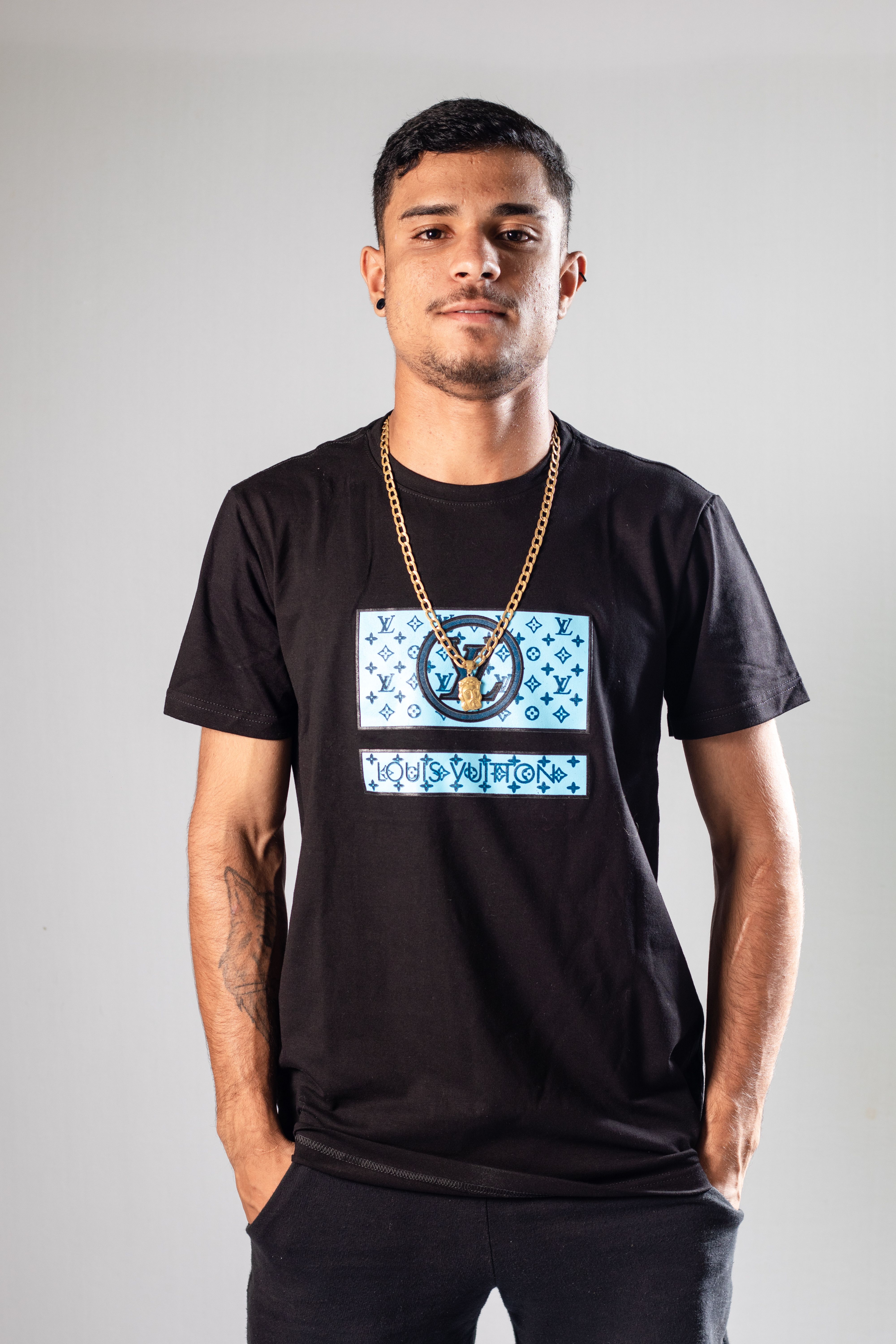 Confident young man wearing a black t-shirt with a golden necklace, standing in a studio.