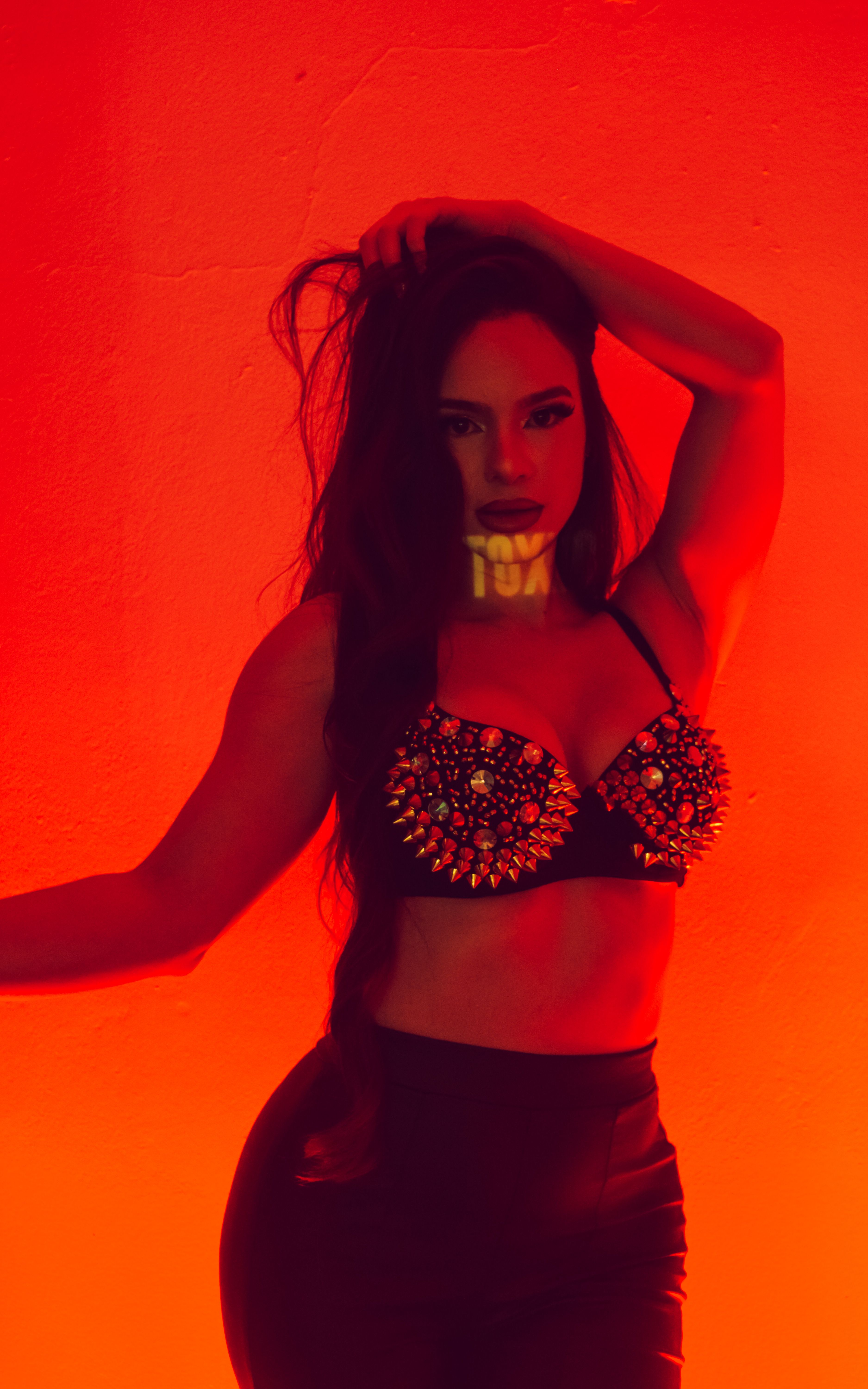 Fashion portrait of a woman posing confidently against a bold orange background.
