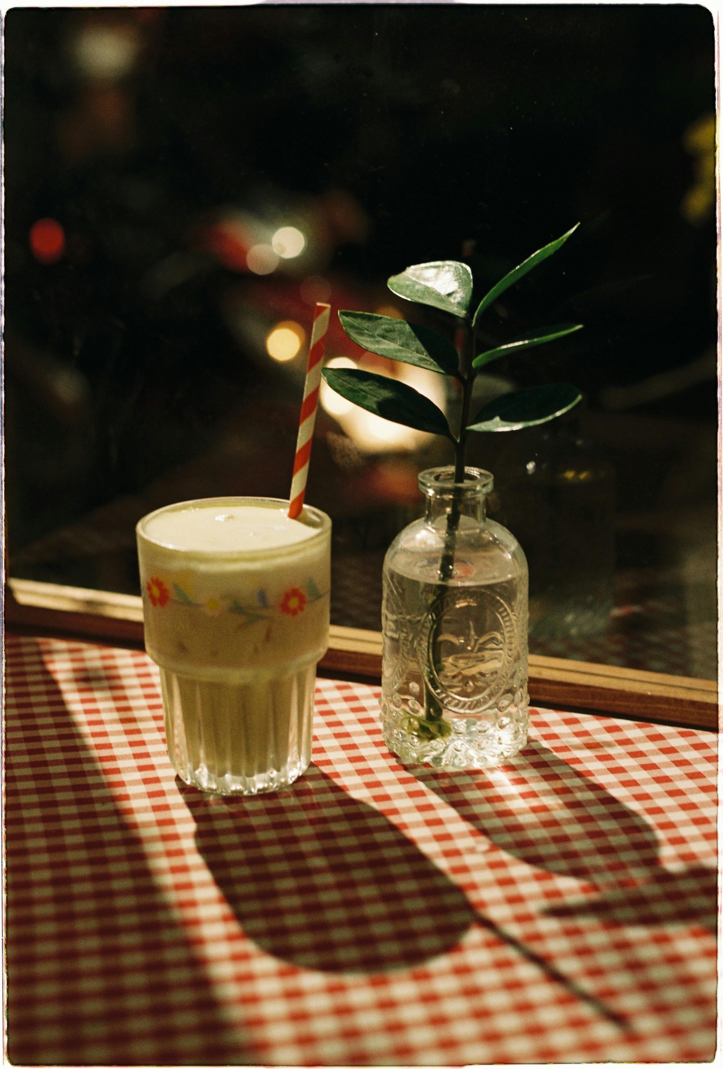 Vintage-style photo of a drink with straw and plant on a checkered tablecloth, ideal for lifestyle themes.