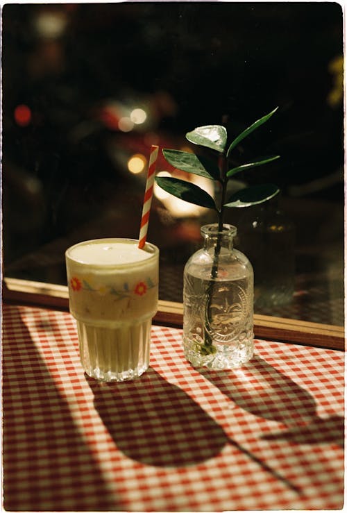 A Cocktail in a Glass with a Straw and a Plant in a Glass Vase 