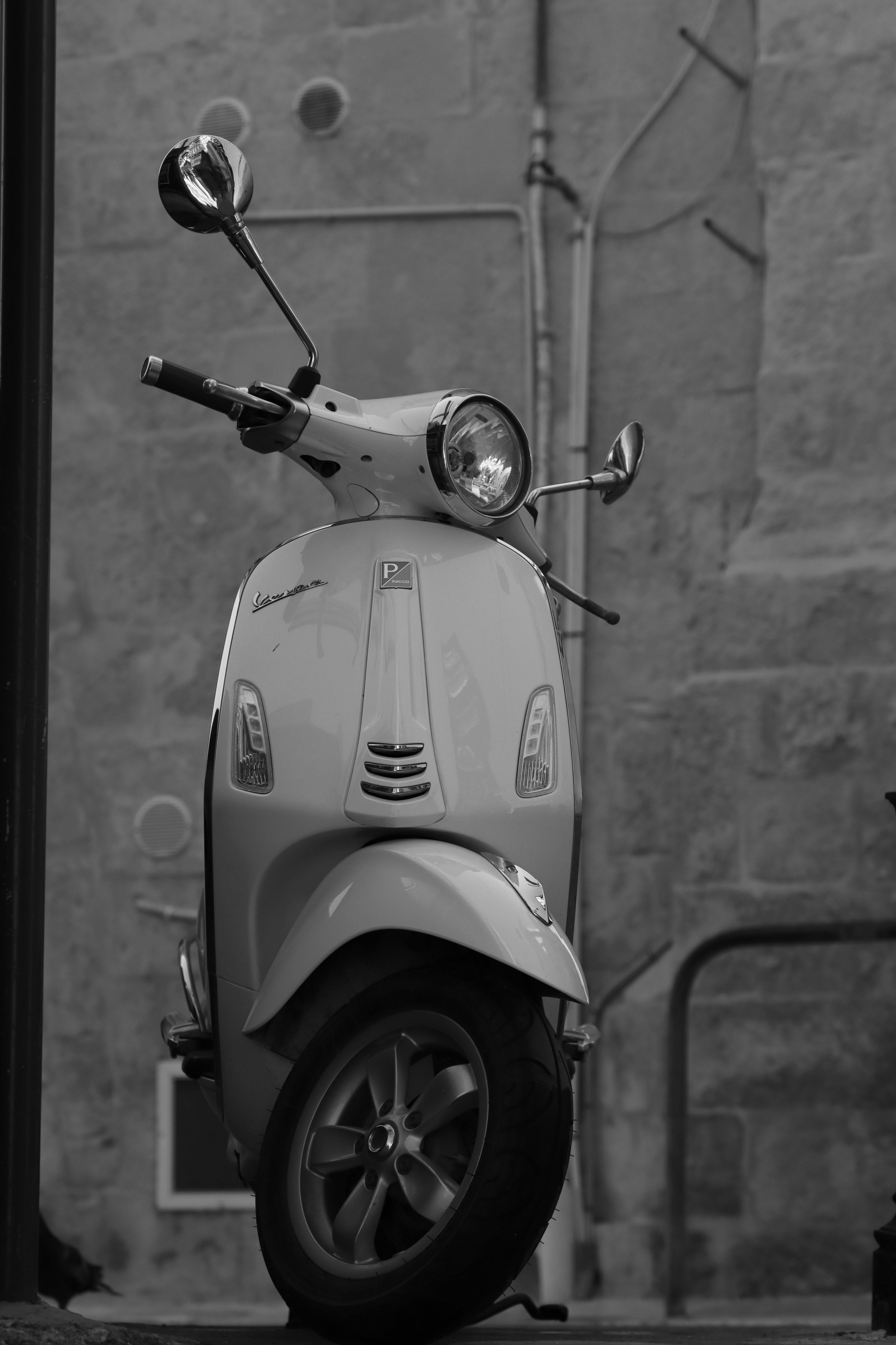 Free Black and white photo of a Vespa scooter parked in an urban street of Malta. Stock Photo