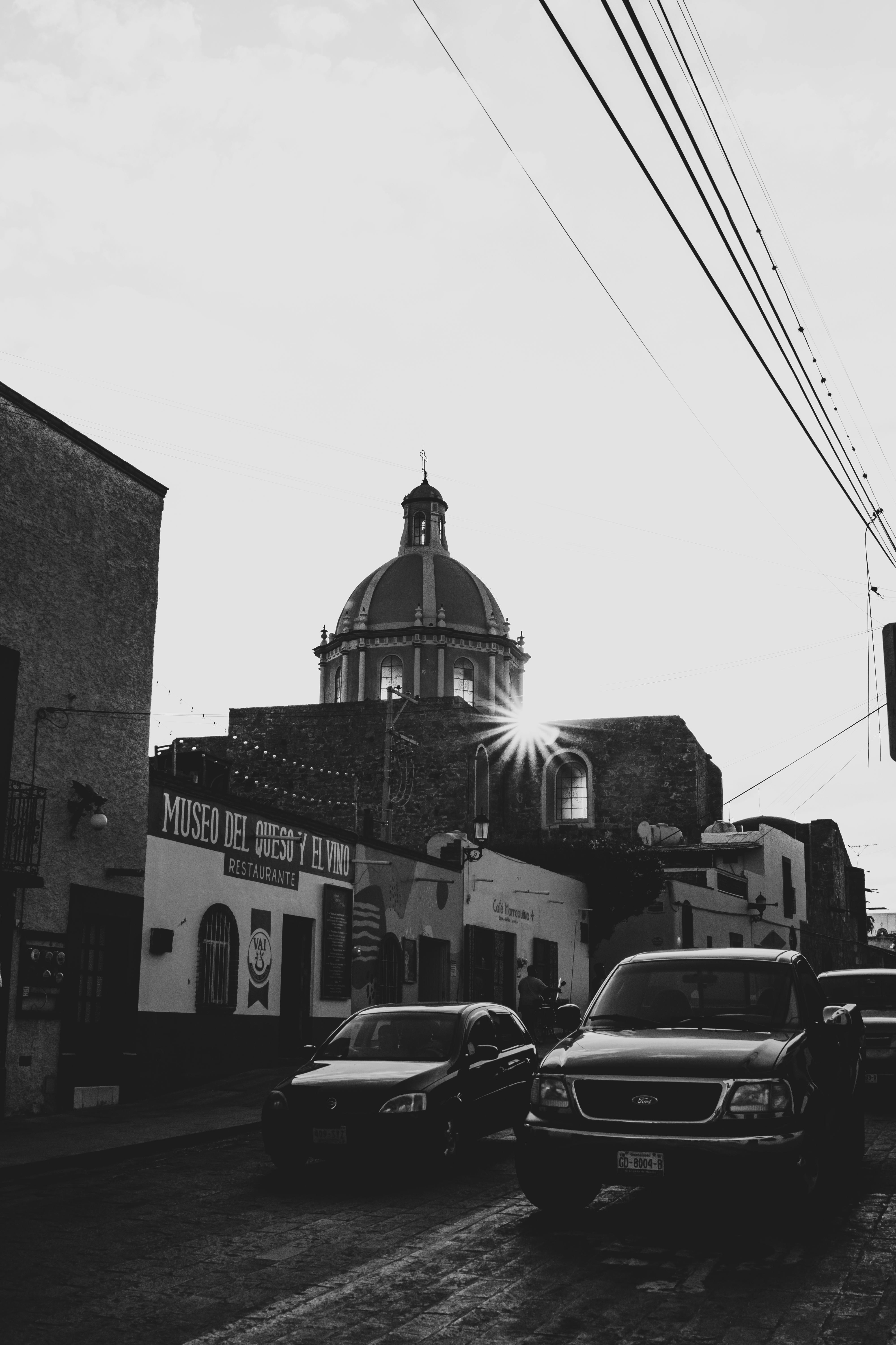 Dramatic black and white street view of Tequisquiapan with church and cars under the sun.