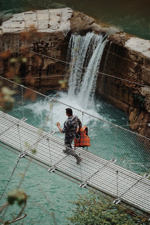 Man Walking on a Wooden Bridge Above a Waterfall 