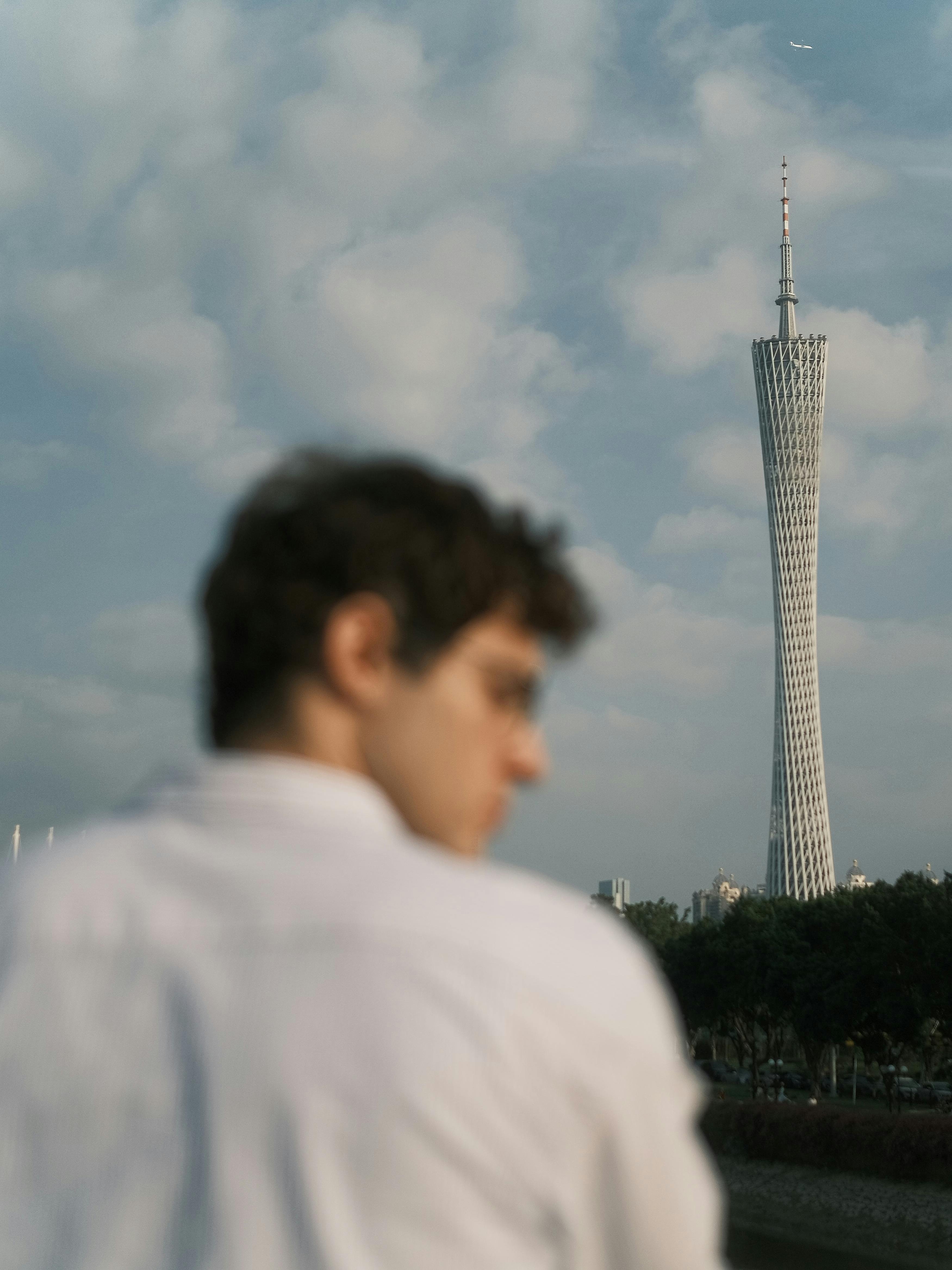 Canton Tower rises against a cloudy sky with a defocused man in the foreground, creating a unique urban scene.