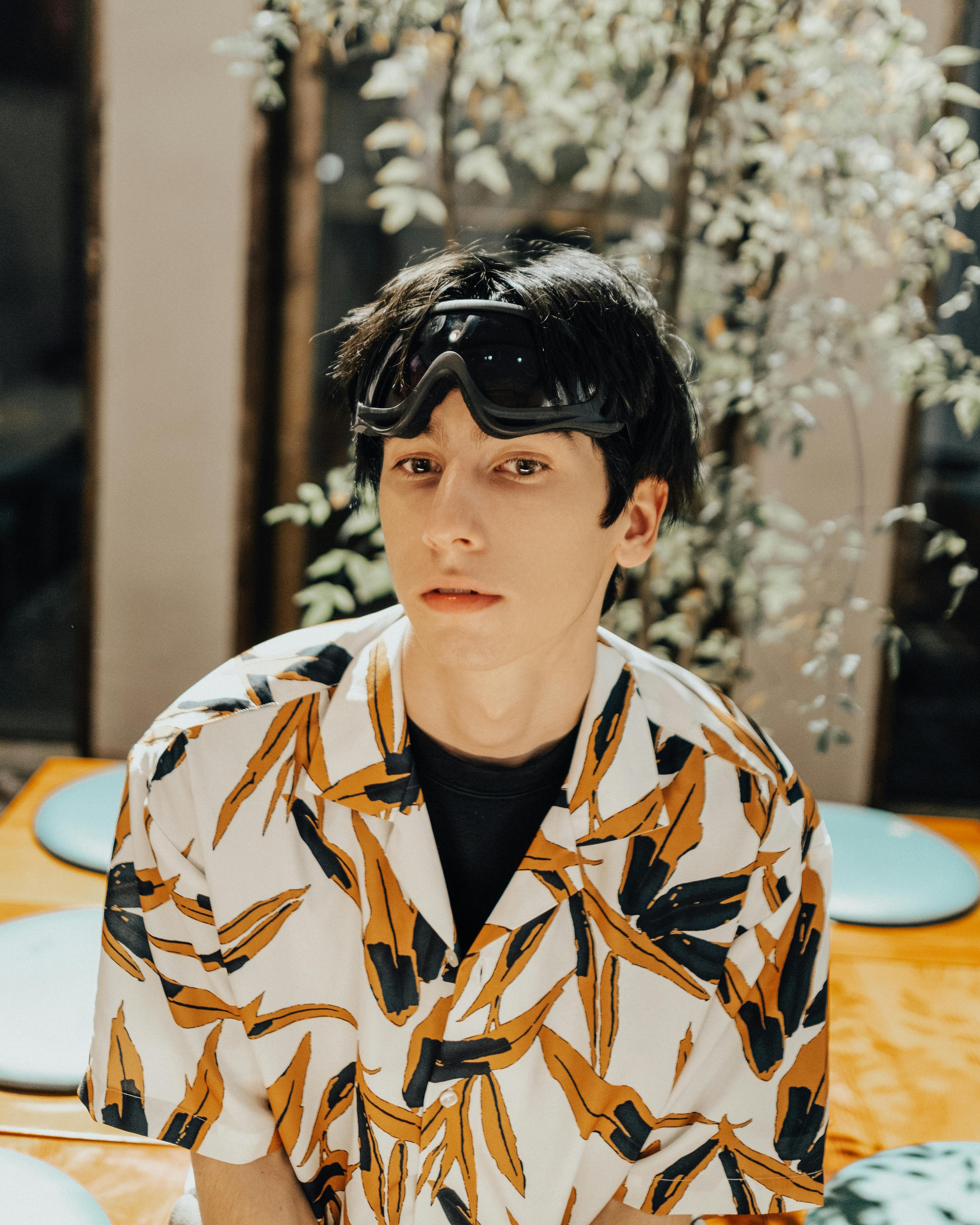 Young man in fashion-forward shirt wearing goggles, exuding contemporary style.