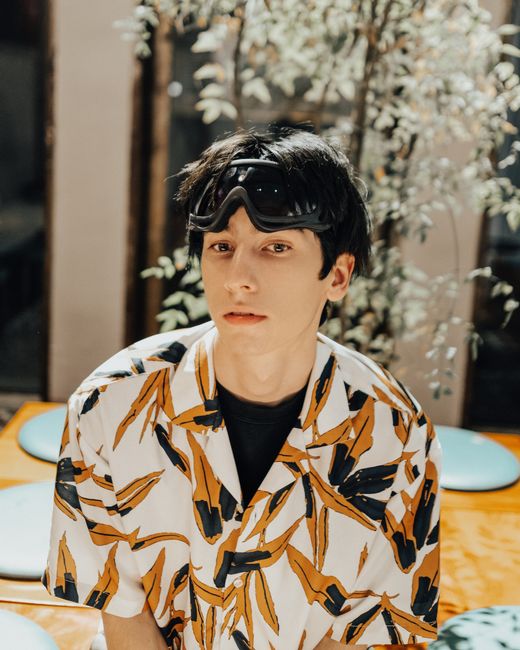 Young man in fashion-forward shirt wearing goggles, exuding contemporary style.