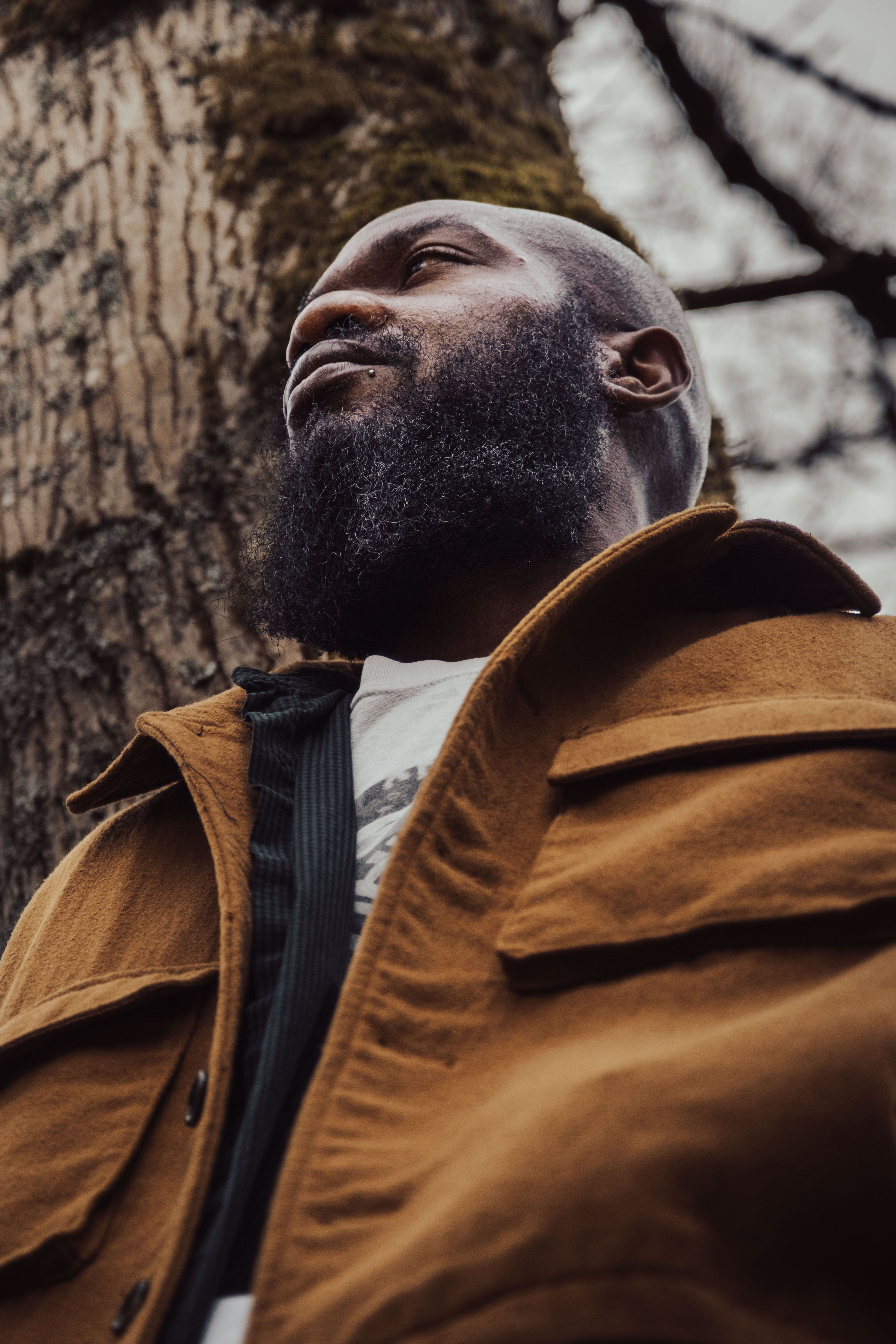 A low-angle portrait of a stylish man with a beard, set in Vancouver forest.