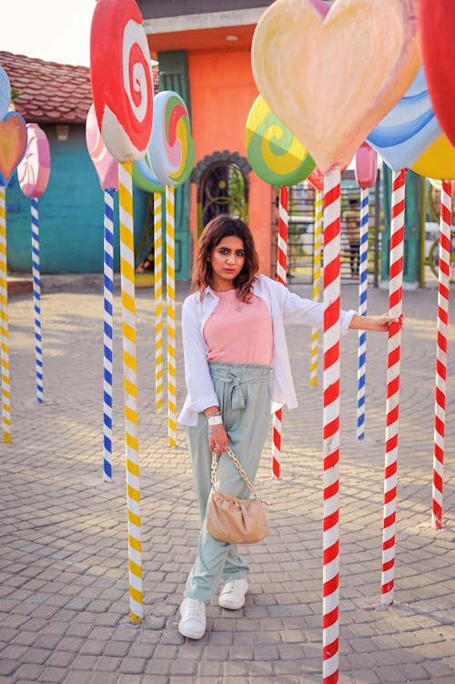 Young Woman Standing between Colorful Decorations in the Shapes of Lollipops in City 