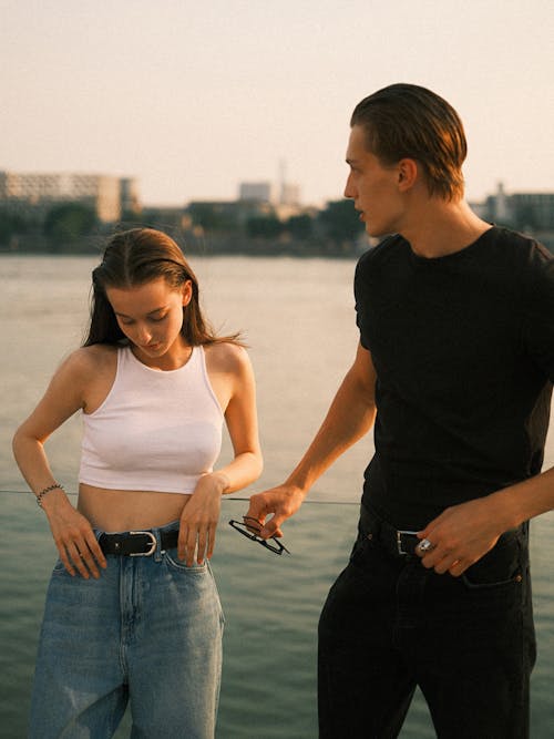 Young Man and Woman in Fashionable Outfits Standing near Water 