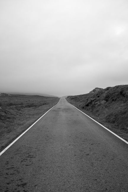A serene black and white image of an empty rural road stretching into the distance.