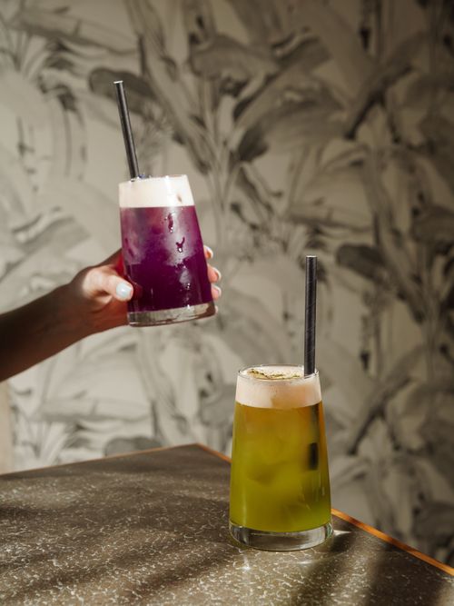 Free Vibrant purple and green cocktails with straws held against a patterned wall. Stock Photo