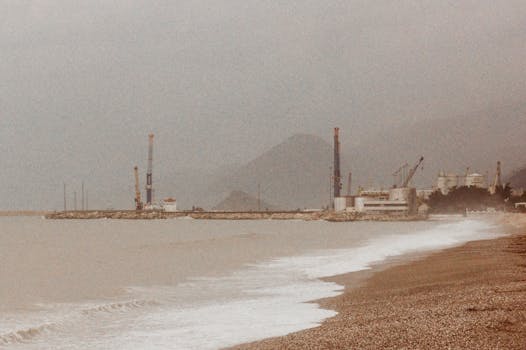 Misty seashore with industrial cranes and buildings in foggy weather, creating a moody, vintage atmosphere.