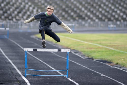 A young man jumping over a hurdle on a track