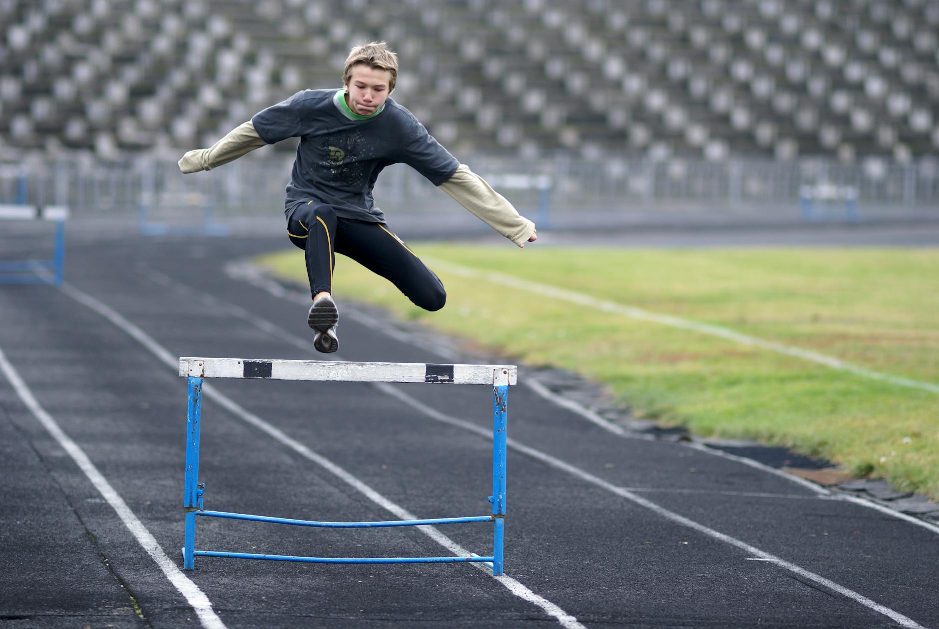 A young athlete hurdles during a practice session on an outdoor stadium track.