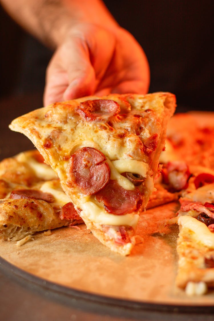 A Person Holding A Slice Of Pizza