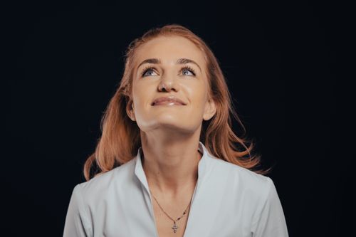 Free A joyful woman with blonde hair gazes upwards against a dark background, embodying optimism and confidence. Stock Photo