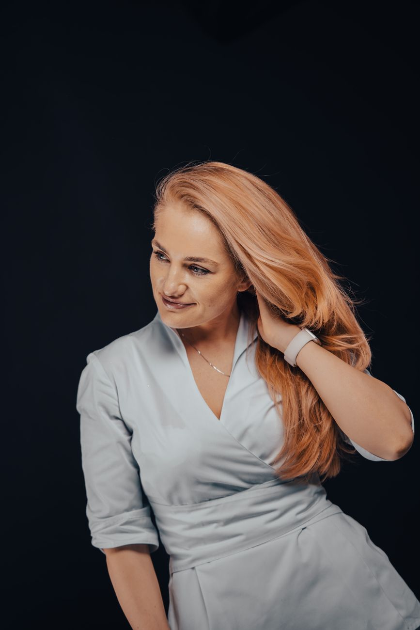 A redhead woman wearing a blue dress, smiling and posing in a studio setting. Elegant casual style.
