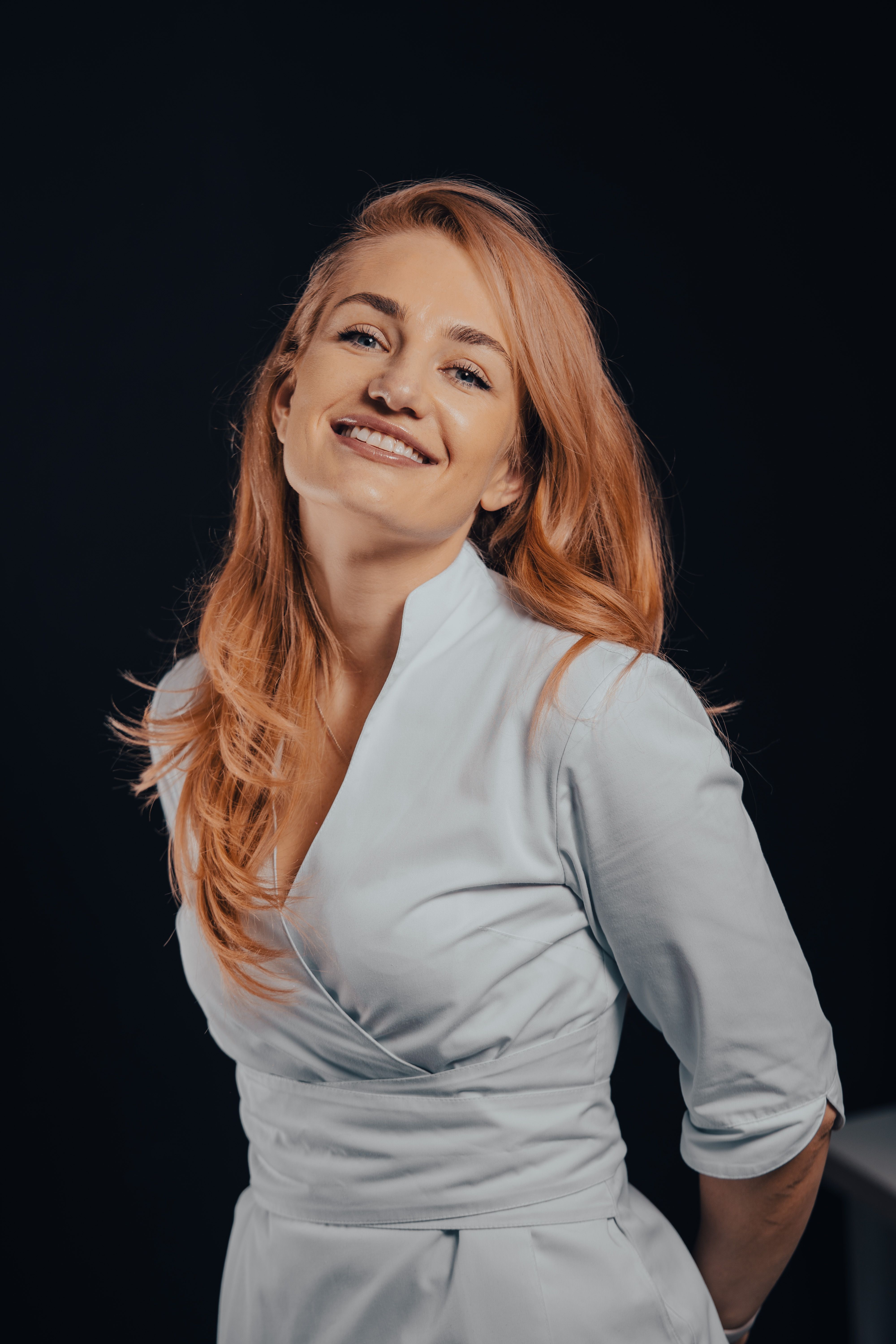 Portrait of a blonde woman smiling confidently against a dark backdrop.