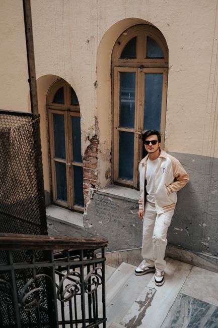 Young man in sunglasses poses stylishly on a vintage urban staircase.