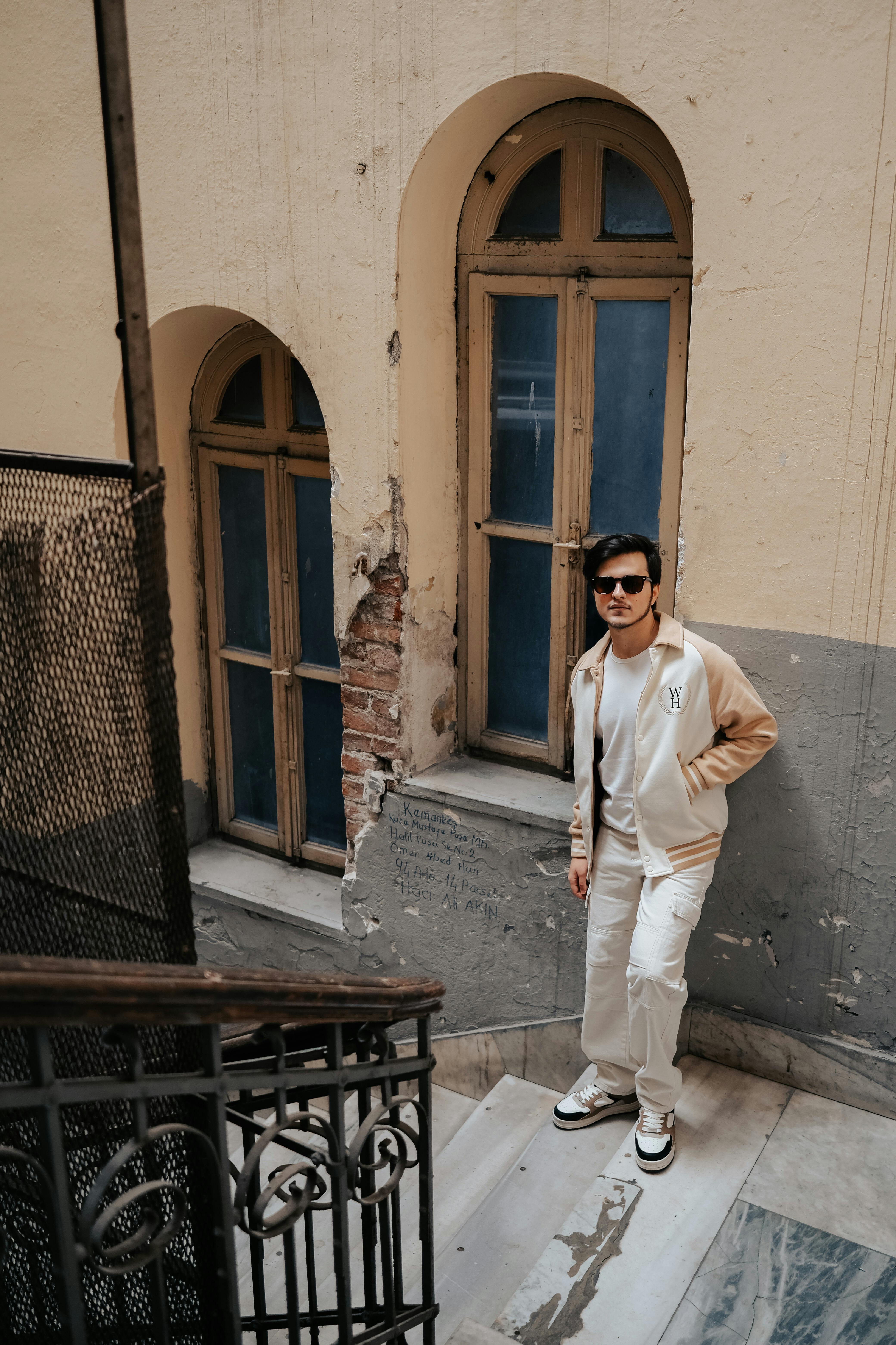 Free Young man in sunglasses poses stylishly on a vintage urban staircase. Stock Photo