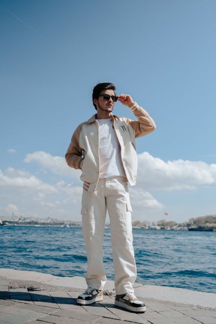Stylish man posing confidently by the seaside, wearing sunglasses and casual attire.