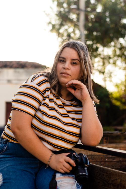 Free A relaxed portrait of a blonde woman in a striped shirt posing with a camera outdoors. Stock Photo