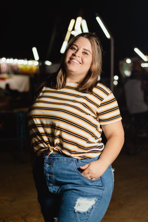 Free Young woman smiling brightly at a nighttime event, dressed casually in a striped shirt and jeans. Stock Photo