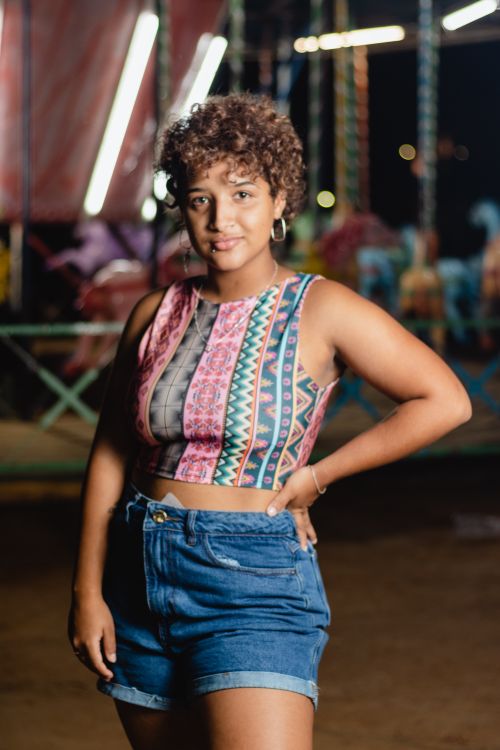 Free Stylized portrait of a woman with curly hair standing confidently at a night carnival setting. Stock Photo